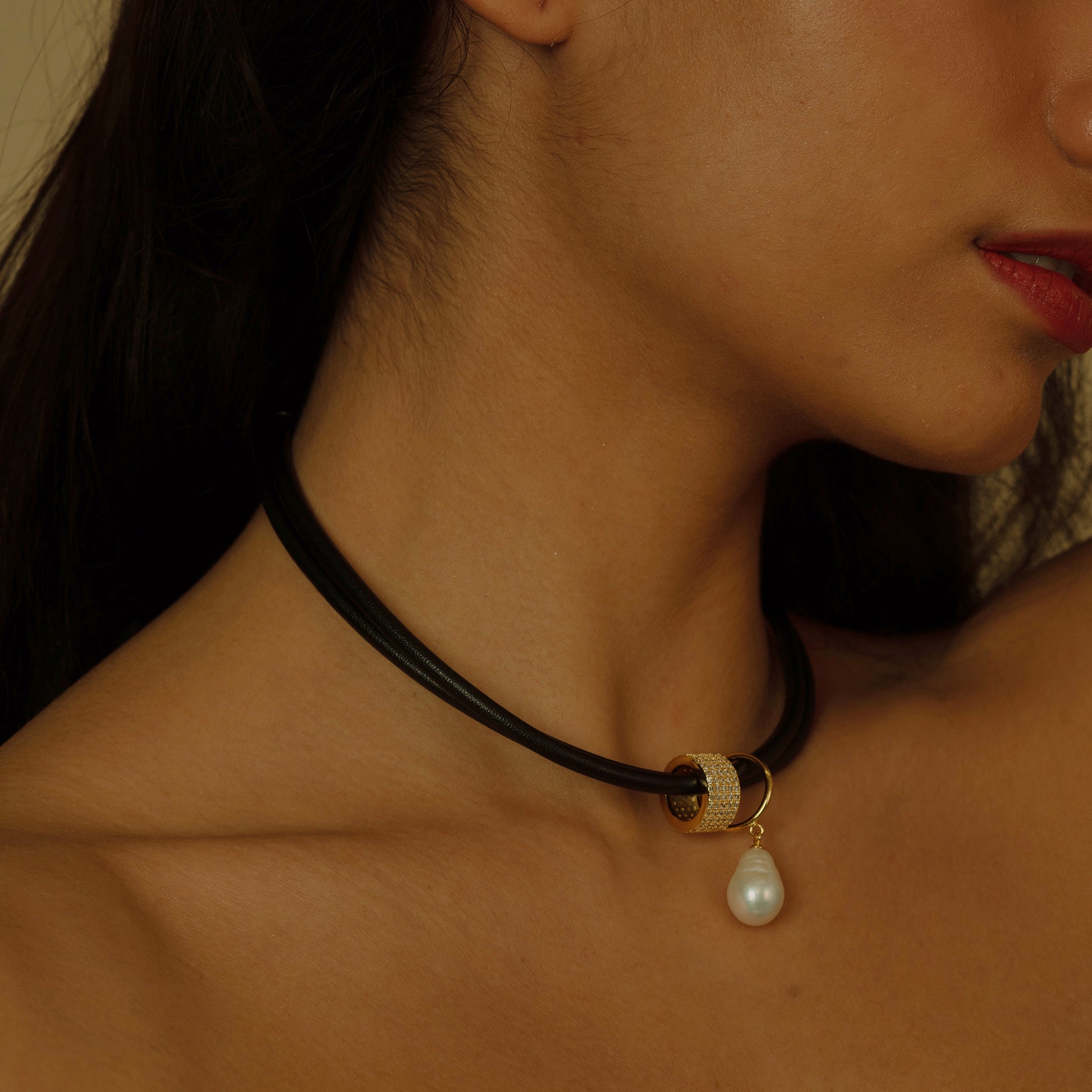 This necklace brings together the contrasting textures of smooth black leather and a single lustrous pearl, accented with a zirconia-encrusted bead. It's a bold piece that redefines elegance with a modern twist.